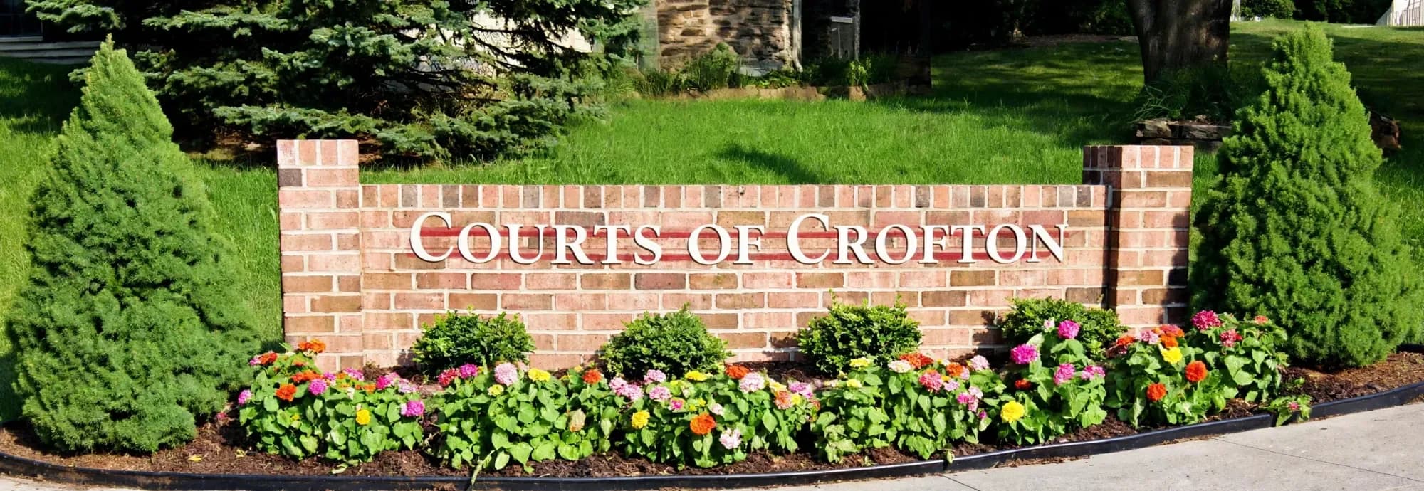 The brick Courts of Crofton sign with flowers in front